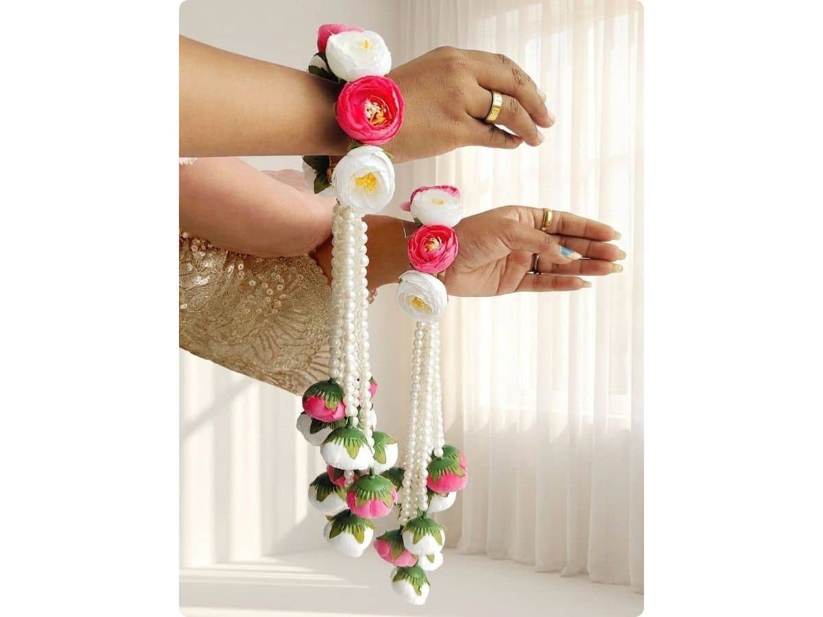 Pink and white flowers worn on a bride's wrists, with long white pearl strings and pink and white flower buds hanging below each hand
